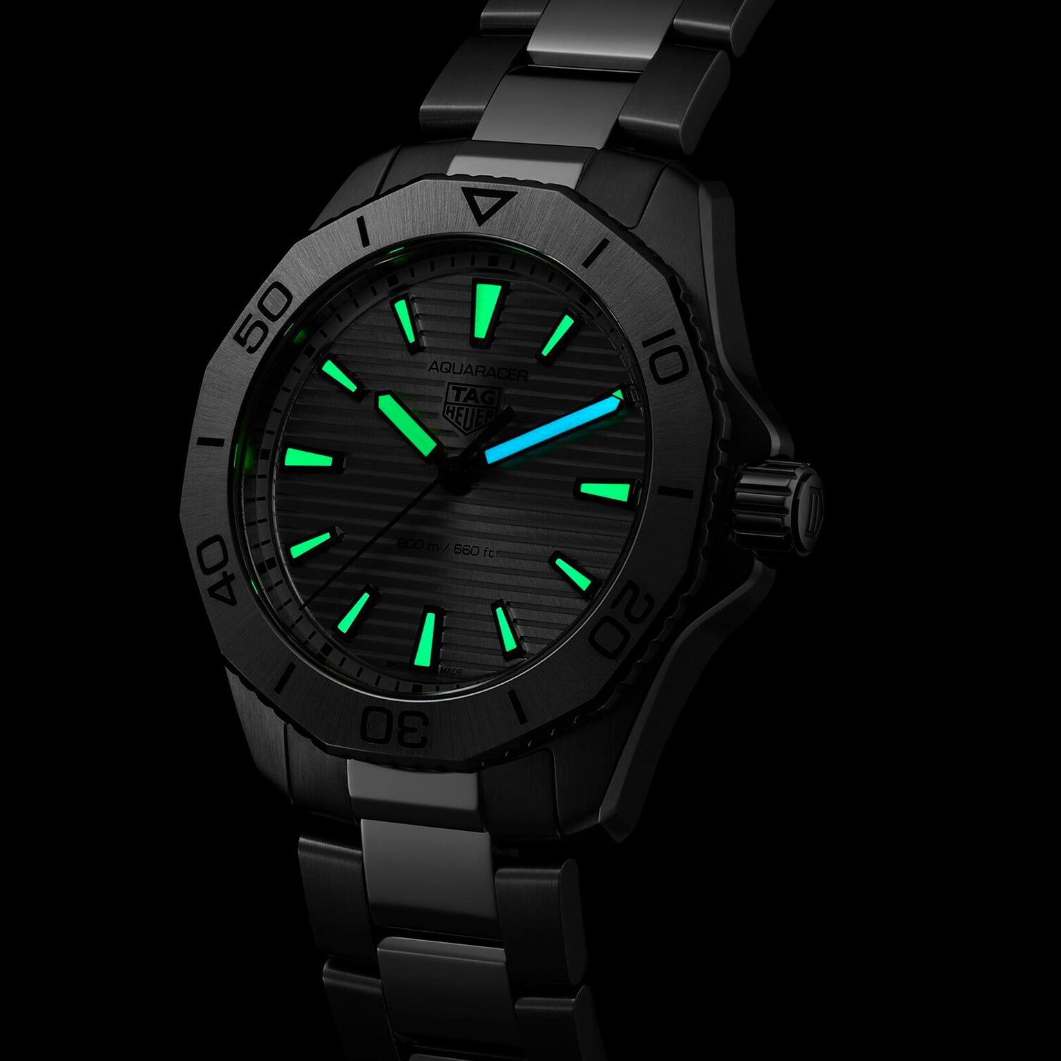 A TAG Heuer Aquaracer Professional 200 watch in stainless steel, featuring luminous green and blue markers on the dial and hands, is displayed against a black background.