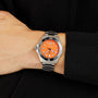 A wrist wearing the TAG Heuer Aquaracer Professional 300 Orange Diver, a silver and black watch with an orange face, with a black sleeve in the background.