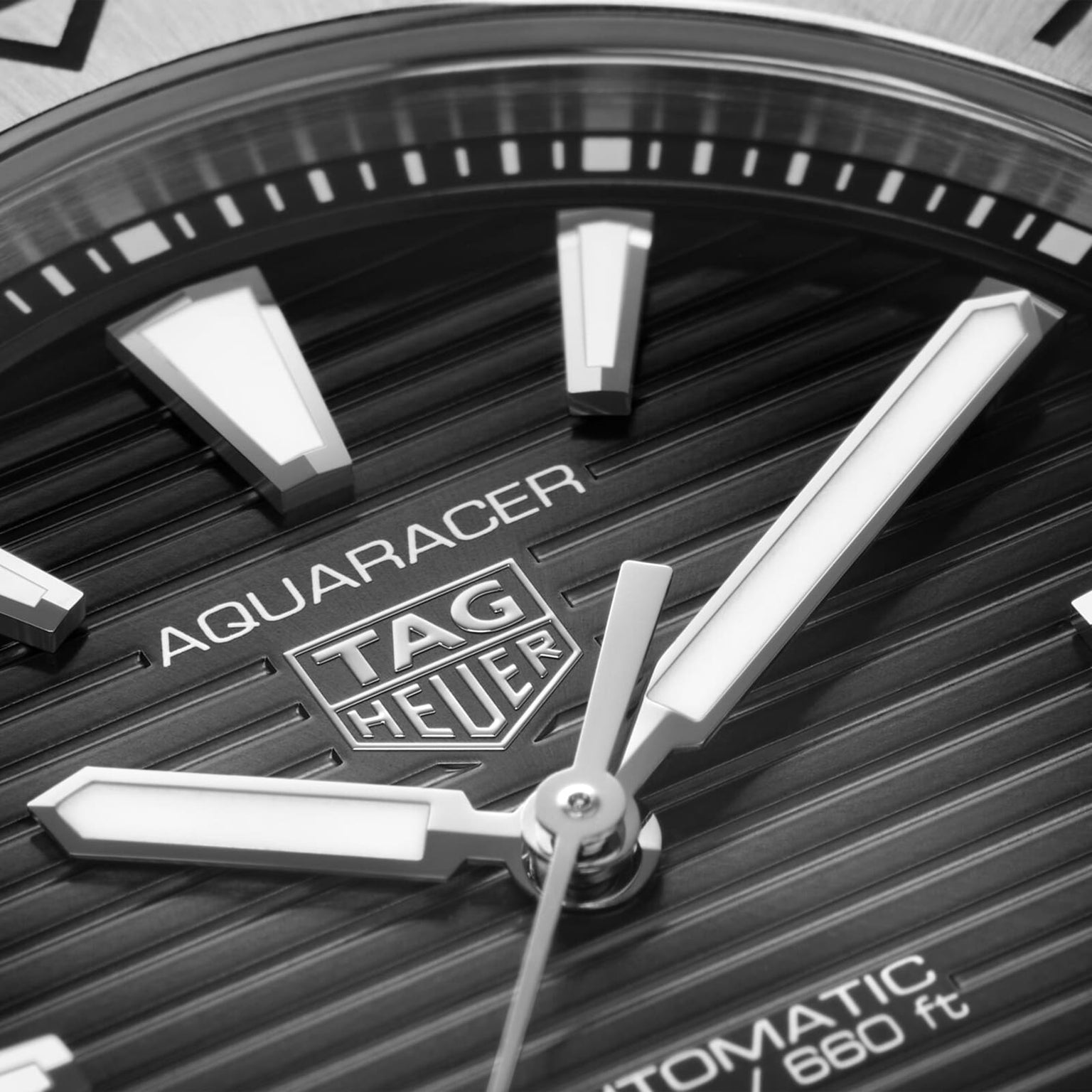 Close-up of a TAG Heuer Aquaracer Professional 200 Date watch face, featuring the TAG Heuer logo, hour markers, and partially visible hands on a textured dial.