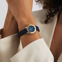 A person in a beige blazer showcases a TAG Heuer Aquaracer Professional 200 Date watch with a gold and blue face and black strap on their left wrist.