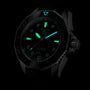 The TAG Heuer Aquaracer Professional 300 Date diving watch is displayed in a dark setting, showcasing its black design, glowing green hour markers and hands, luminous blue triangle at 12 o’clock, and striking blue lagoon dial accents.