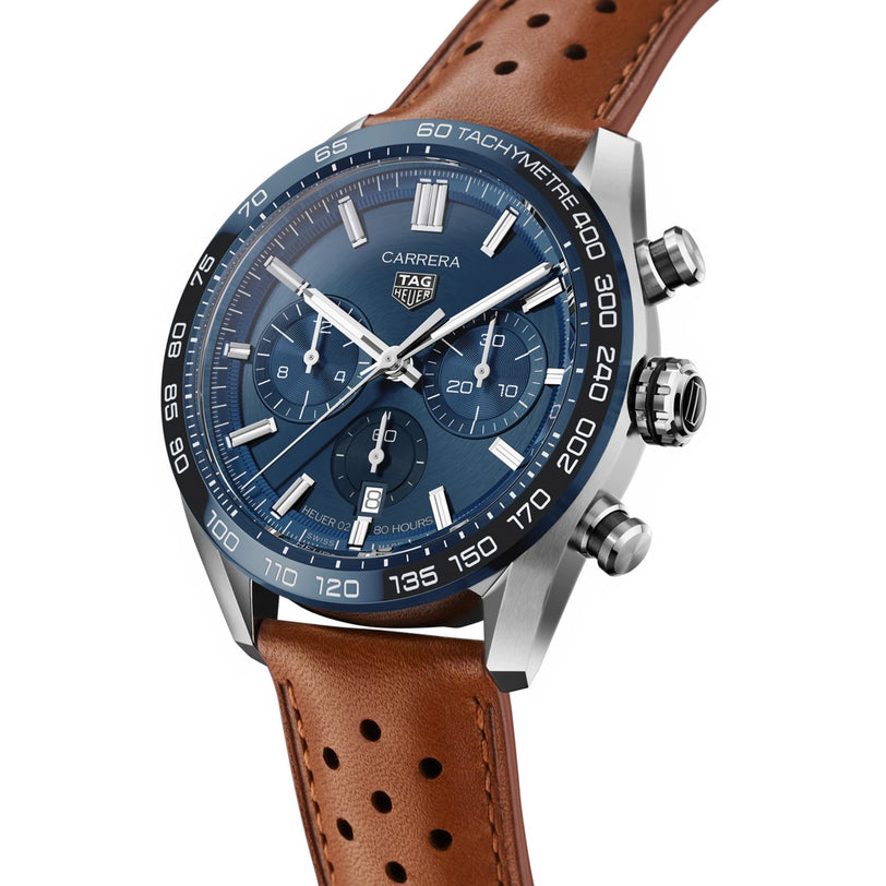 The TAG Heuer Carrera Chronograph features a blue dial with three subdials, a tachymeter bezel, and a brown perforated leather strap—a tribute to the brand’s motor-racing legacy.