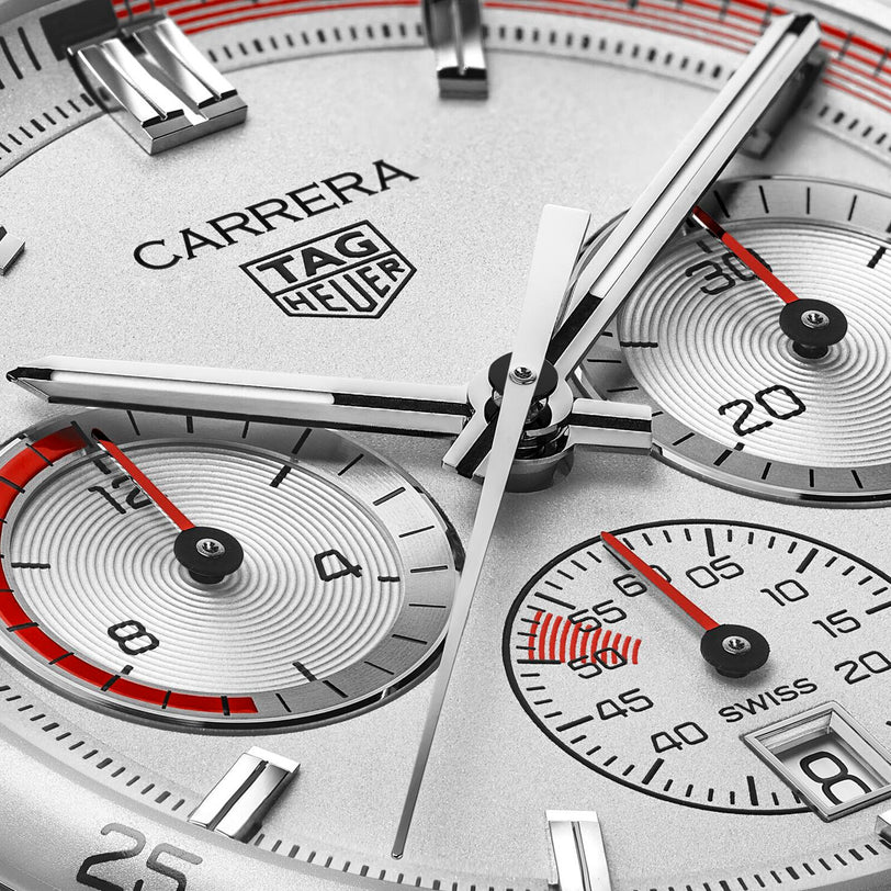Close-up of a TAG Heuer Special Edition Carrera Chronosprint x Porsche watch face featuring three subdials, silver hands, and red accents on a silver background, displaying the time at about 1:46:34.