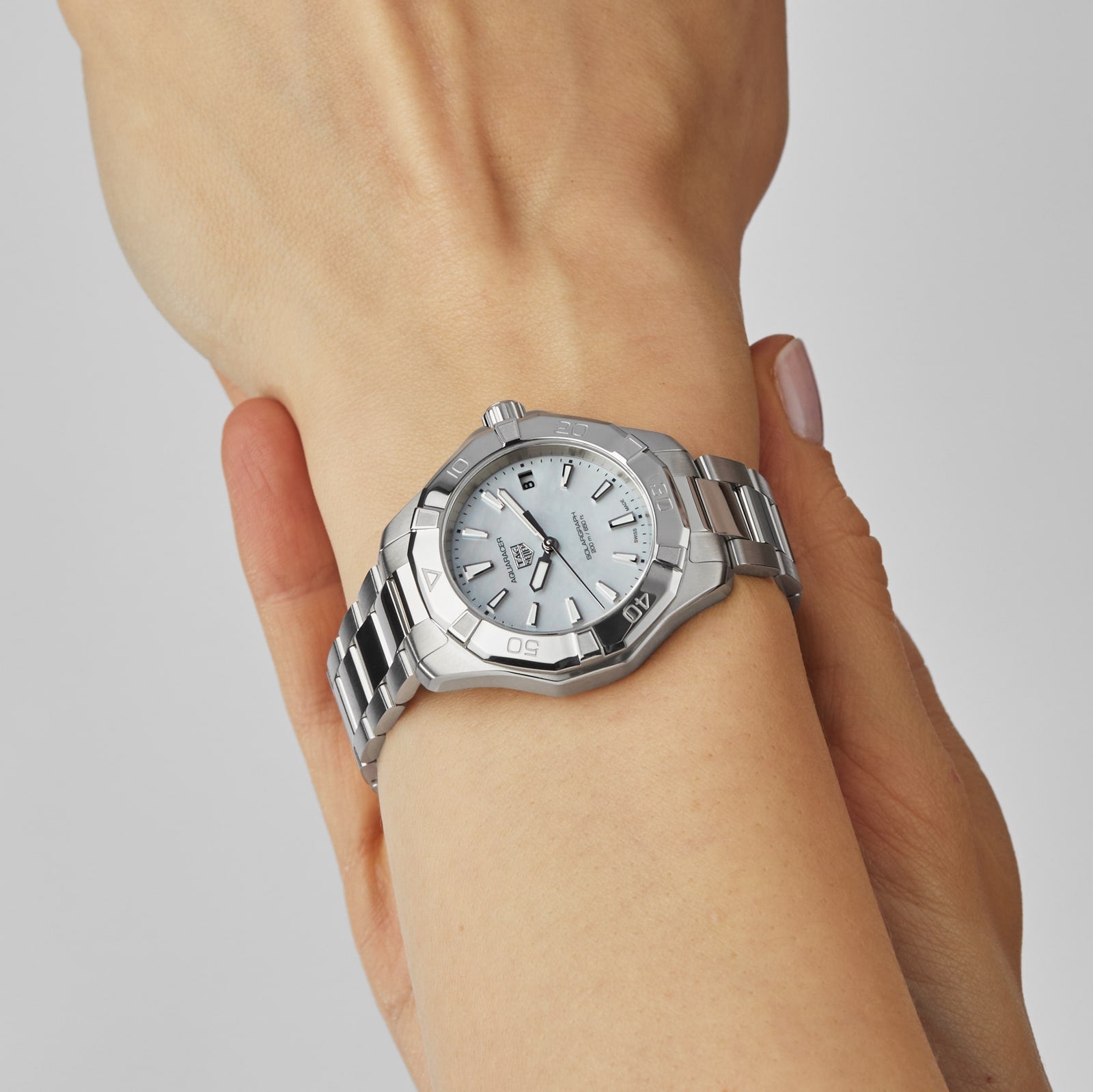 A close-up of the TAG Heuer Aquaracer 200 Professional Solargraph, a silver solar-powered watch with a white face and metal band, worn on the left wrist and gently held by the right hand—showcasing its elegant design.