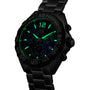 A TAG Heuer Formula 1 Chronograph with a black dial, glowing green hour markers and hands, and a metal band is displayed in a dark setting.