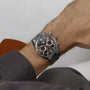 A TAG Heuer Carrera Chronosprint x Porsche Rallye Limited Edition watch with a silver case and a black and red dial is worn on a person’s wrist.