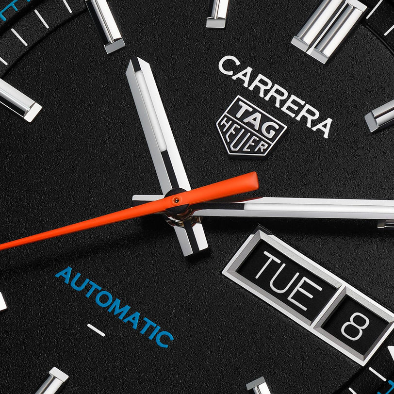 Close-up of a TAG Heuer Carrera Day-Date watch face displaying the date, day, time, and an orange second hand.