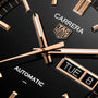 Close-up of the TAG Heuer Carrera Day-Date watch face, featuring gold hands and day-date displays on a black background.