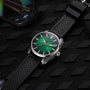 The H. Moser & Cie Pioneer Centre Seconds Cosmic Green wristwatch with a green dial and black strap rests on a textured black surface next to a pair of sunglasses.