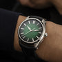 A wrist wearing the H. Moser & Cie Pioneer Centre Seconds Cosmic Green analog watch with a black strap, set against a dark background.