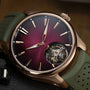 The H. Moser & Cie Pioneer Tourbillon Burgundy features a burgundy dial, gold accents, a green strap, and showcases its visible tourbillon mechanism for a luxurious look.