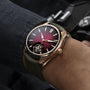 The H. Moser & Cie Pioneer Tourbillon Burgundy, featuring a red gradient dial and visible tourbillon, is worn on a persons wrist.