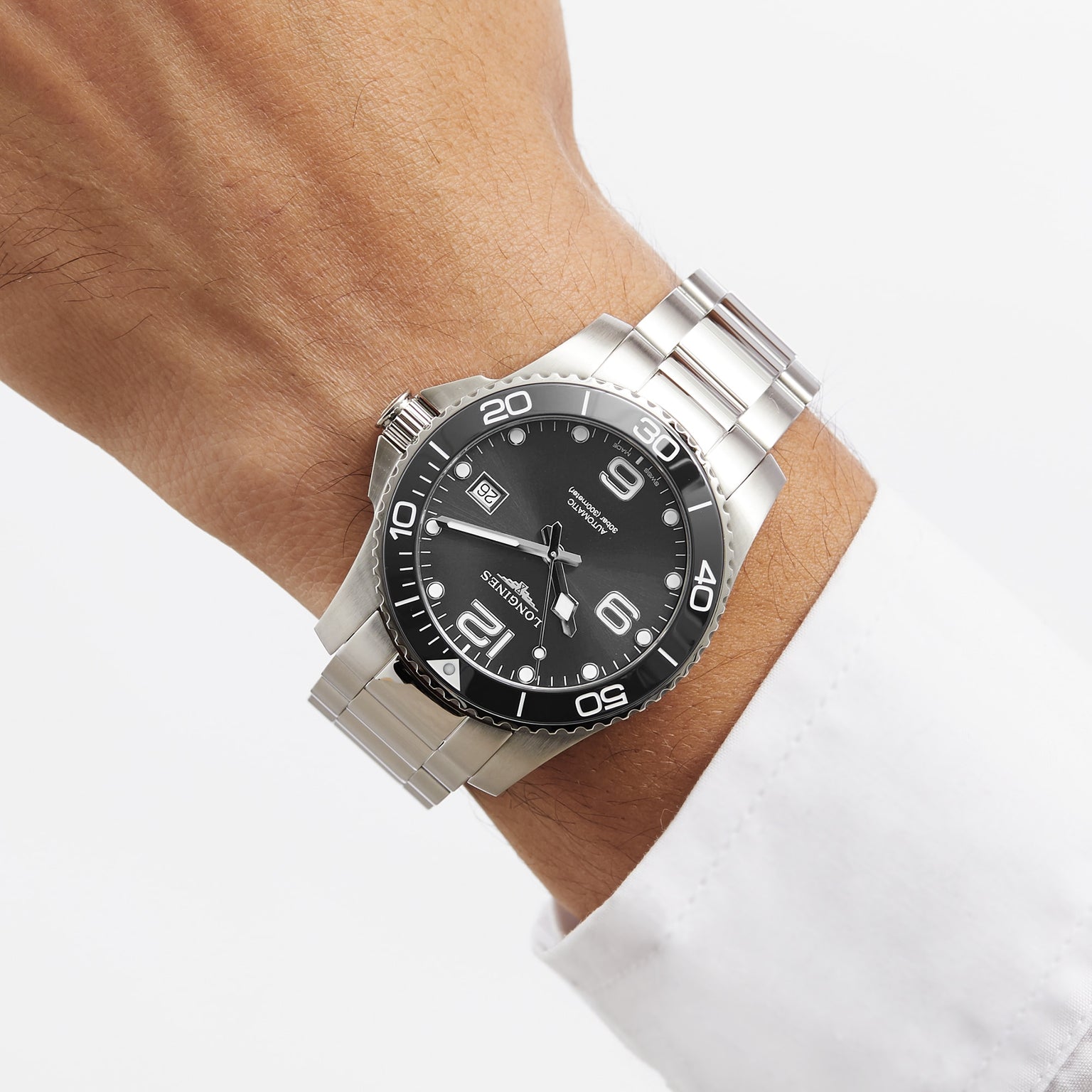 A Longines HydroConquest silver wristwatch with a black face and metal band is worn on a persons wrist with a white dress shirt.