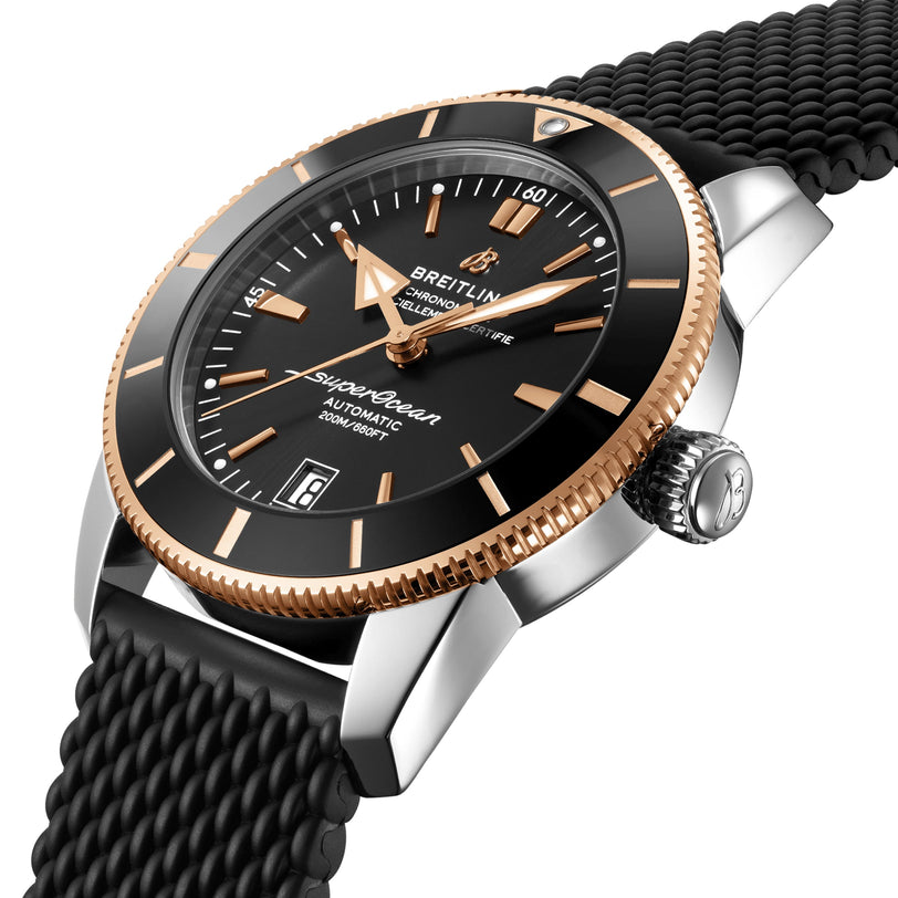 The Breitling Superocean Heritage B20 Automatic 42 features a black dial, gold bezel, date window, and black textured strap. Shown at an angle, it runs on the Breitling B20 movement and is designed for water resistance.
