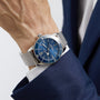 A person in a blue suit jacket wears a Breitling Superocean Heritage B20 Automatic 44, featuring a silver mesh strap, blue dial, and stainless steel case.