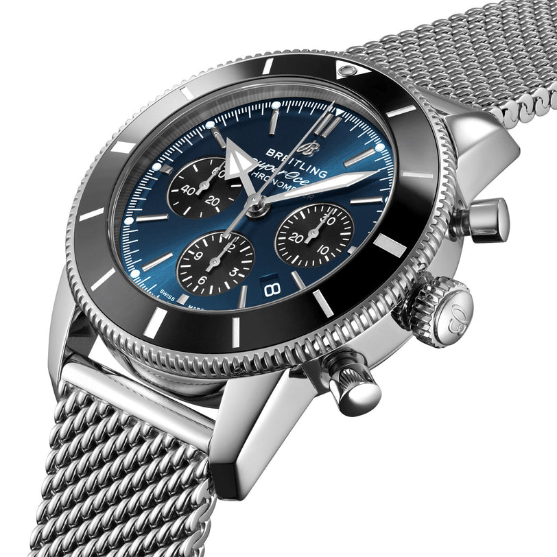 A close-up of the Breitling Superocean Heritage B01 Chronograph 44 featuring a blue dial with three subdials, powered by the Breitling 01 calibre, black bezel, and a mesh stainless steel band.