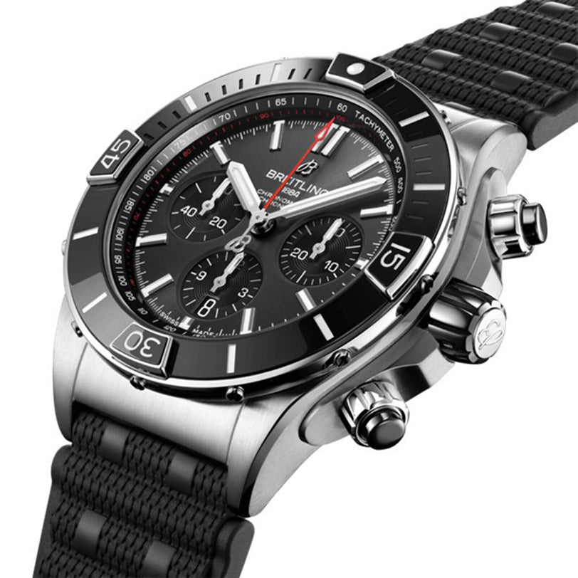 A close-up of the Breitling Super Chronomat B01 44 highlights its stainless steel case, black dial with three subdials, rotating bezel, and textured black strap—showcasing the precision of this mechanical chronograph.