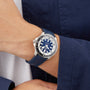 A person wears a blue and silver Breitling Superocean Automatic 44 with a blue strap and dark blue jacket, highlighting the water-resistant automatic watch.