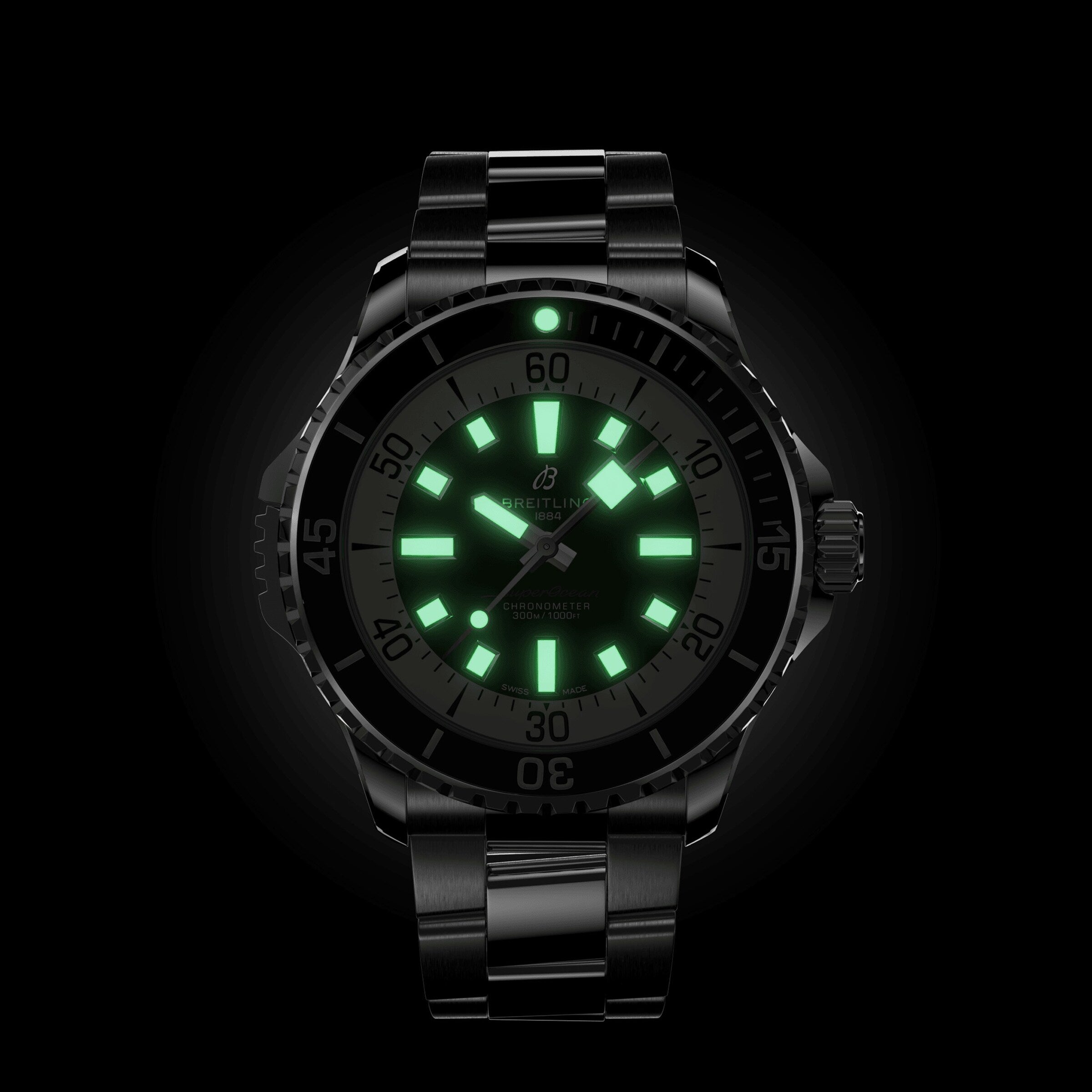 The Breitling Superocean Automatic 46 is a black wristwatch with a metal band, glowing green hour markers and hands on a dark dial, inspired by the iconic 1960s Slow Motion design.