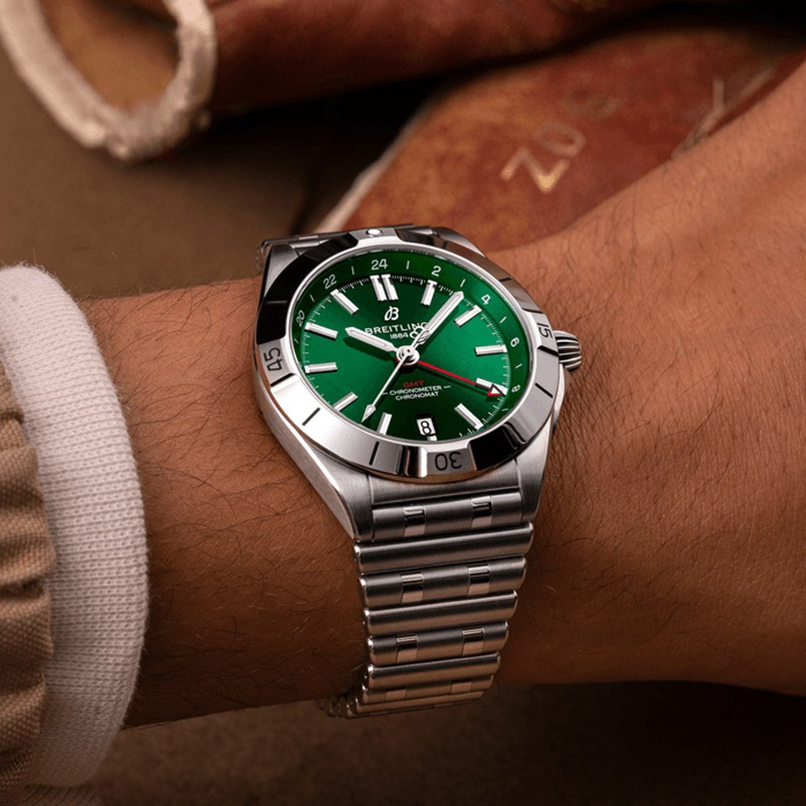 A close-up of a person wearing a Breitling Chronomat Automatic GMT 40 with an emerald dial and stainless steel bracelet, showing the time at 10:10.