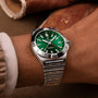 A close-up of a person wearing a Breitling Chronomat Automatic GMT 40 with an emerald dial and stainless steel bracelet, showing the time at 10:10.