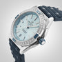 A Breitling Super Chronomat Automatic 38 wristwatch with a silver case, ice blue dial, diamond-set bezel, and dark blue textured strap is displayed on a light gray background.