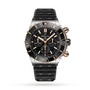 Breitling Super Chronomat B01 44 mechanical chronograph with a black and gold bezel, black dial with three subdials, date window at 6 oclock, and a textured black strap.