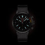 The Breitling Top Time B01 Chevrolet Corvette is a black racing chronograph with a mesh strap, luminous hour markers, multiple subdials, and a tachymeter bezel, powered by the Manufacture Calibre 01 and shown against a dark background.