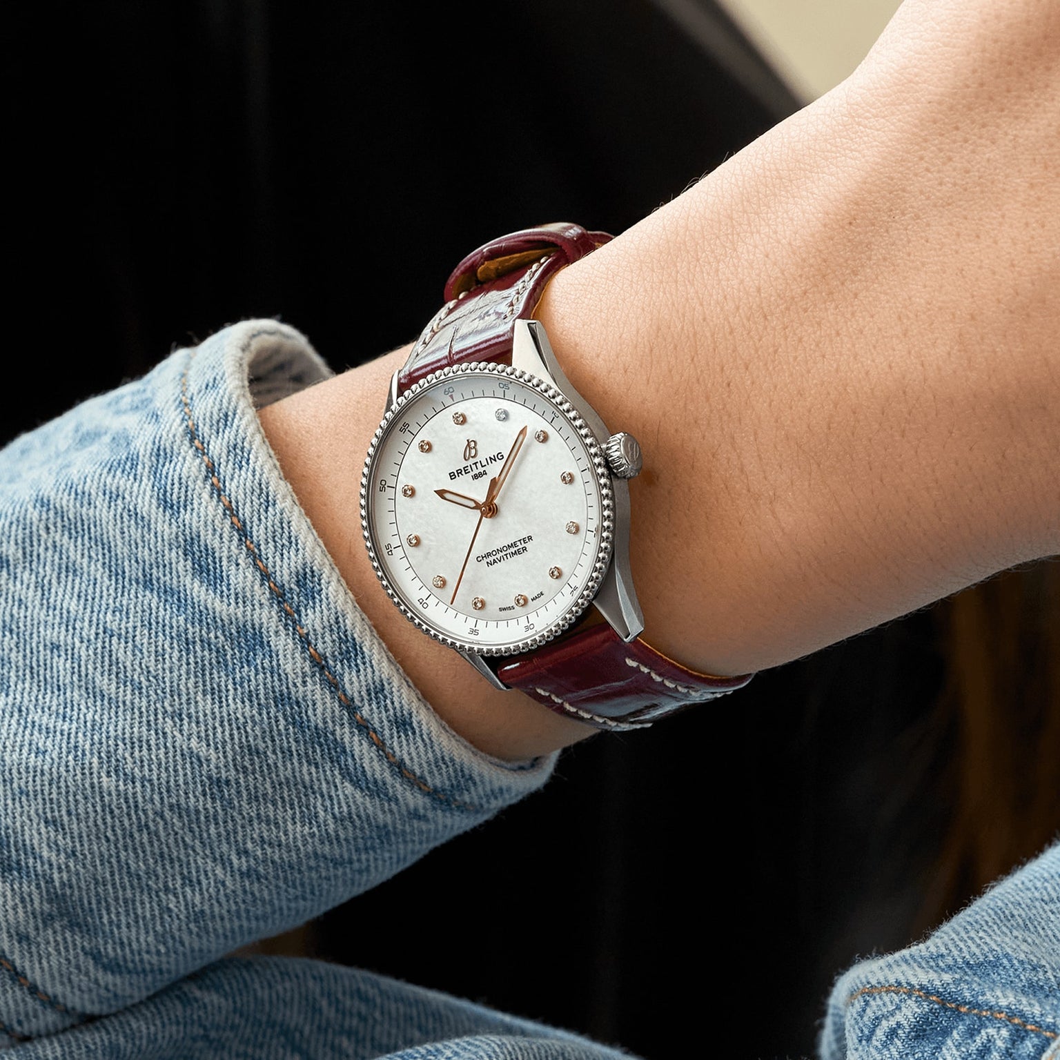 A person wearing a Breitling Navitimer 32 with a white dial, diamond hour markers, and brown leather strap, styled in a light blue denim jacket.