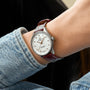 A person wearing a Breitling Navitimer 32 with a white dial, diamond hour markers, and brown leather strap, styled in a light blue denim jacket.