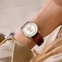 A close-up of a wrist wearing the Breitling Navitimer Automatic 36, featuring a silver case, brown leather strap, white dial with silver hour markers, and powered by the Breitling 17 calibre movement.