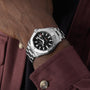 A person wearing a maroon shirt with beige buttons sports a Breitling Avenger Automatic 42 wristwatch, featuring a stainless steel case and a military-inspired black dial with a silver bezel.
