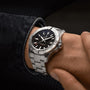 A person wearing a Breitling Avenger Automatic 42 with a military-inspired black dial and silver bracelet on their left wrist.