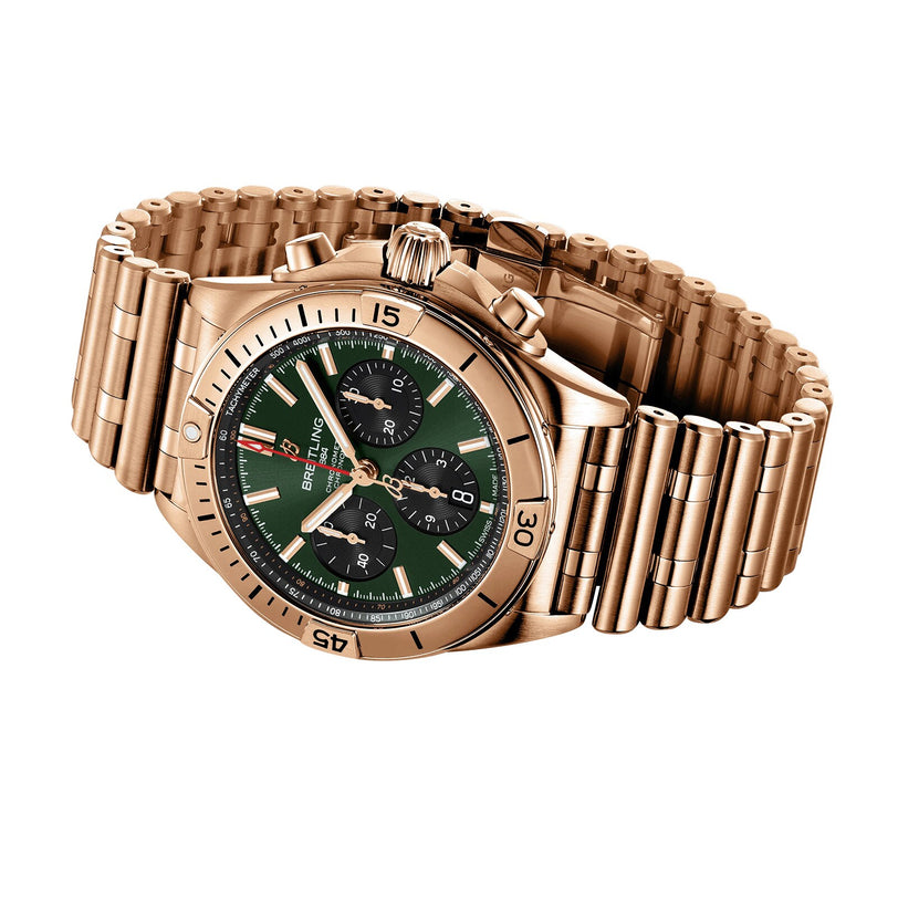 The Breitling Chronomat B01 42 features a gold case, green chronograph dial with three subdials, and a metal link bracelet, displayed at an angle on a white background.