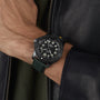Wearing the Breitling Avenger Automatic GMT 44 Night Mission, featuring a black case, green military leather strap, and large white numerals, with a black leather jacket channels classic aviation style.