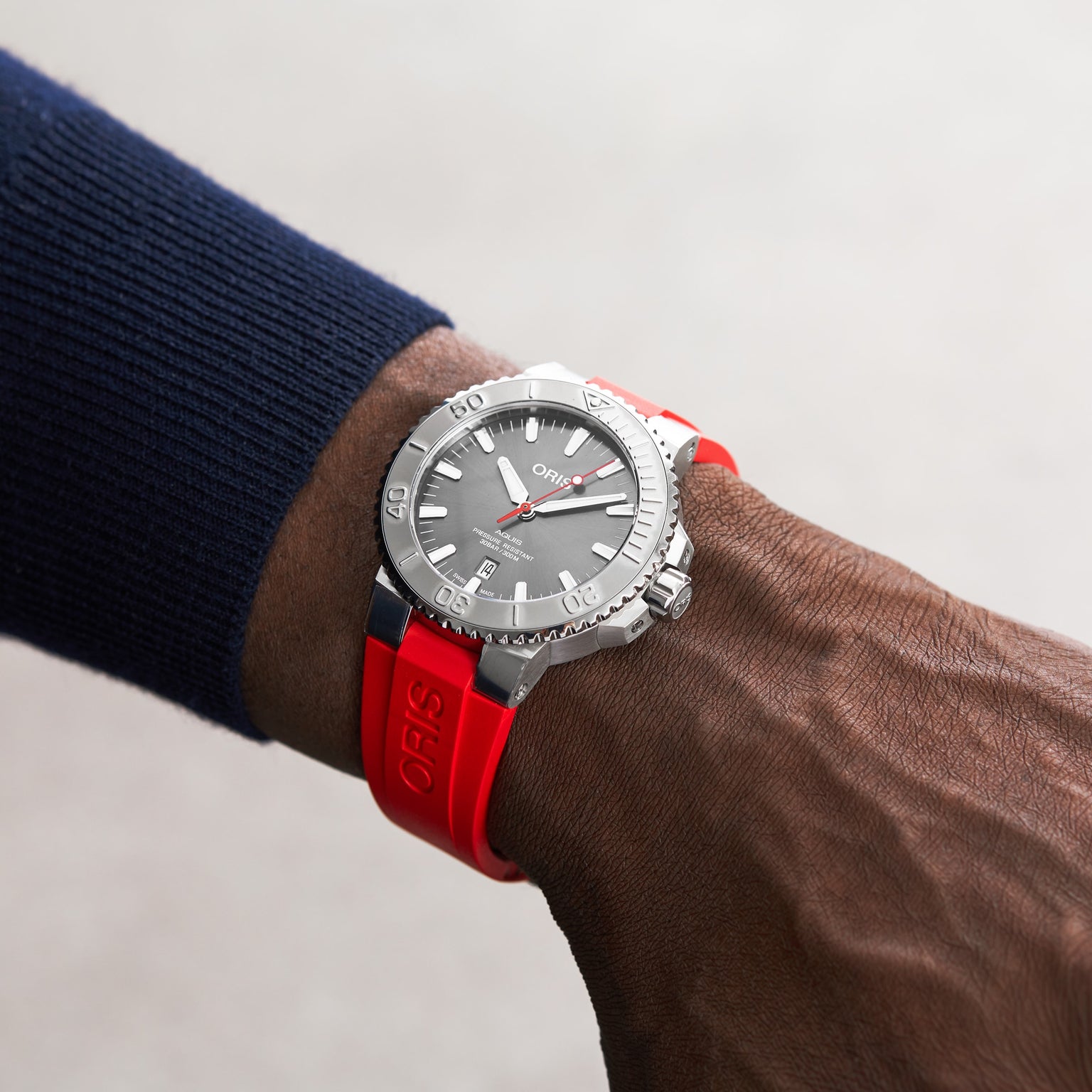 Someone wearing an Oris Aquis Date Relief watch featuring a grey dial and a red silicone strap on their wrist.