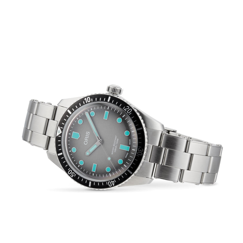 The Oris Divers Sixty‑Five is a stainless steel wristwatch featuring a black bezel and glowing blue hour markers on a gray dial.