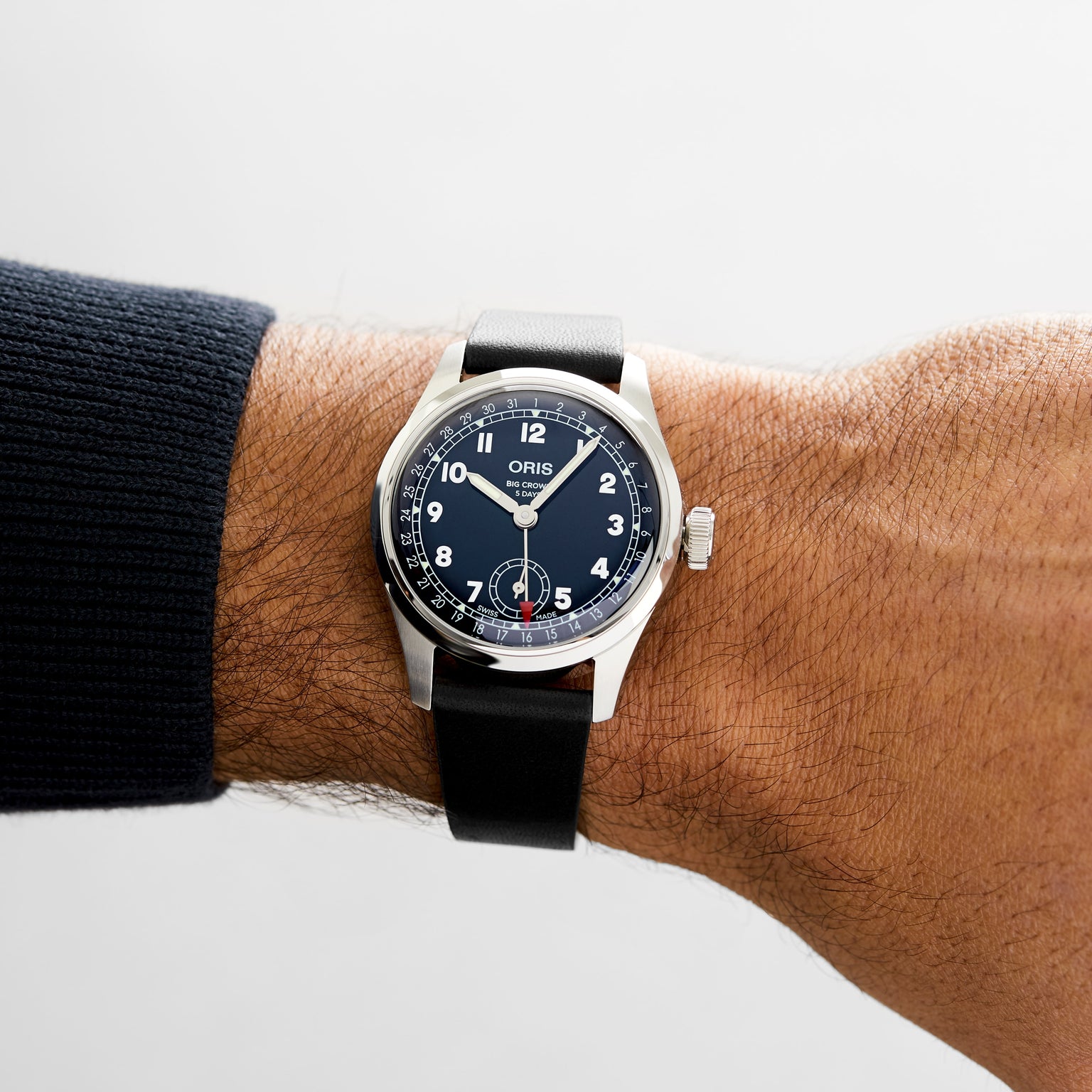 A person wearing an Oris Big Crown Pointer Date Calibre 403 on their left wrist, featuring a black leather strap, black dial with white numerals, and a silver case.