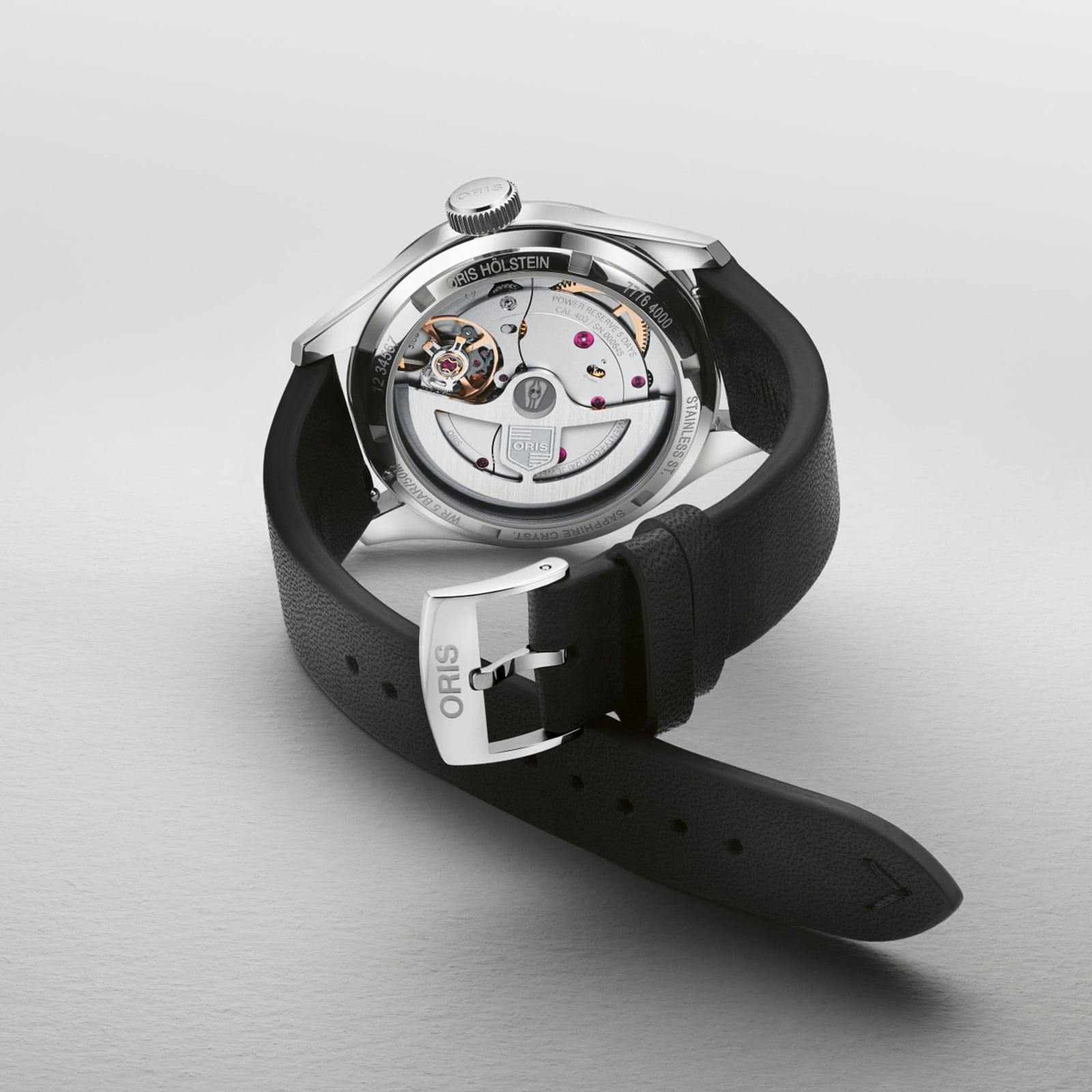 The Oris Big Crown Pointer Date Calibre 403 wristwatch with a black leather strap is displayed face down, revealing its intricate movement and inner workings, with Oris engraved on the buckle.
