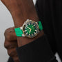 A person wearing an Oris Aquis Date Calibre 400 dive watch with a green rubber strap and gold accents, powered by the Calibre 400 movement, shown on their wrist against a dark long-sleeve shirt.