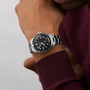 A person wearing the Oris Divers Sixty‑Five 12H Calibre 400 silver wristwatch with a black dial and a burgundy long-sleeve shirt.