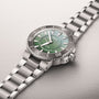The Oris Dat Watt Limited Edition II is a stainless steel watch with a green dial, silver hour markers, and a metal link bracelet, inspired by Wadden Sea conservation, shown against a light background.
