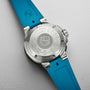 The back of an Oris Aquis Pro 4000M shows engraved specs, Calibre 400 branding, and the Rotation Safety System on its stainless steel case with a blue rubber strap.