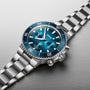 The Oris Aquis Chronograph, a stainless steel wristwatch with a blue dial, ceramic bezel, three subdials, and metallic bracelet, is displayed on a light gray surface to showcase its exceptional water resistance.