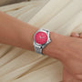 A person’s wrist wears an Oris ProPilot X Miss Piggy Edition watch with a hot pink dial and silver case, set against cream-colored fabric.