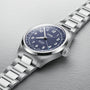 An Oris Big Crown Pointer Date wristwatch with a blue dial, white Arabic numerals, metal bracelet, and Swiss Made automatic movement is displayed on a light textured surface.