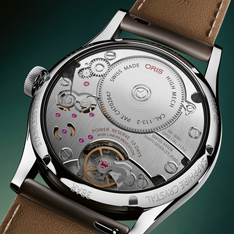 Close-up of a mechanical watch with visible brand name on a dark green background