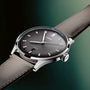 Stainless steel watch with black dial, silver hour markers, and gray leather strap against green background.