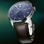 Stainless steel watch with blue dial, moonphase subdial, date window, and brown leather strap.