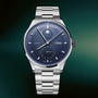 Silver stainless steel watch with dark blue dial, moonphase complication at top, subsidiary dial at bottom, and matching meta